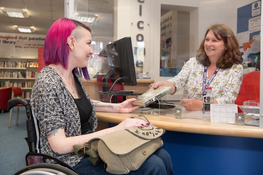 A lady in a library serving a customer who is in a wheelchair